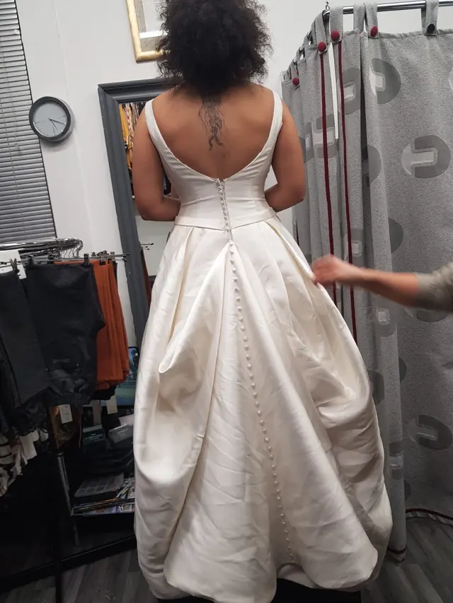 A client in a full ivory satin ballgown in the fitting room while the skirt is adjusted