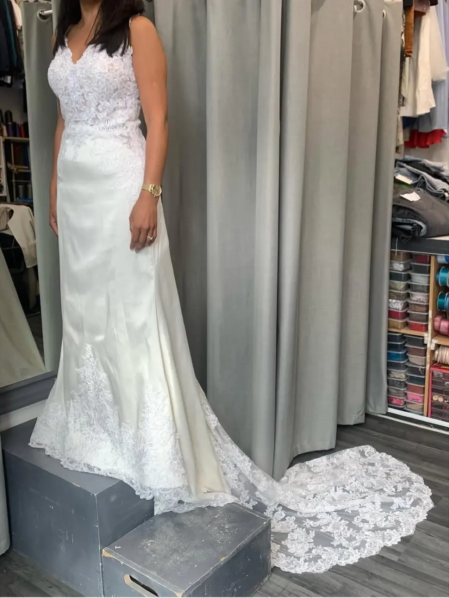 A client in a fitted lace wedding gown with a long train on the fitting platform